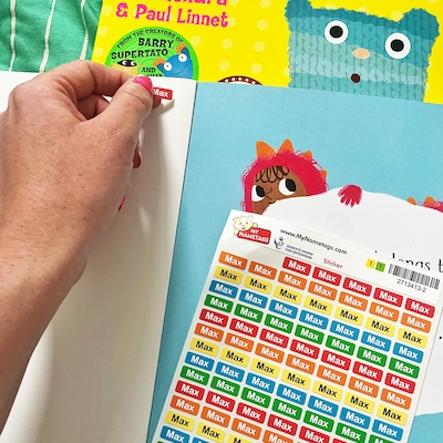 Hand die een ministicker in een prentenboek plakt, naast een vel ministickers