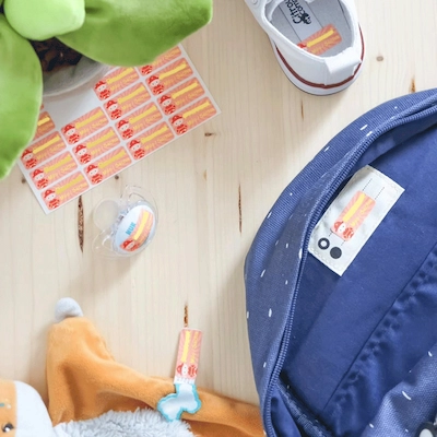 Vellen naamstickers op een tafel met een rugzak, een fopspeen, knuffels en schoenen